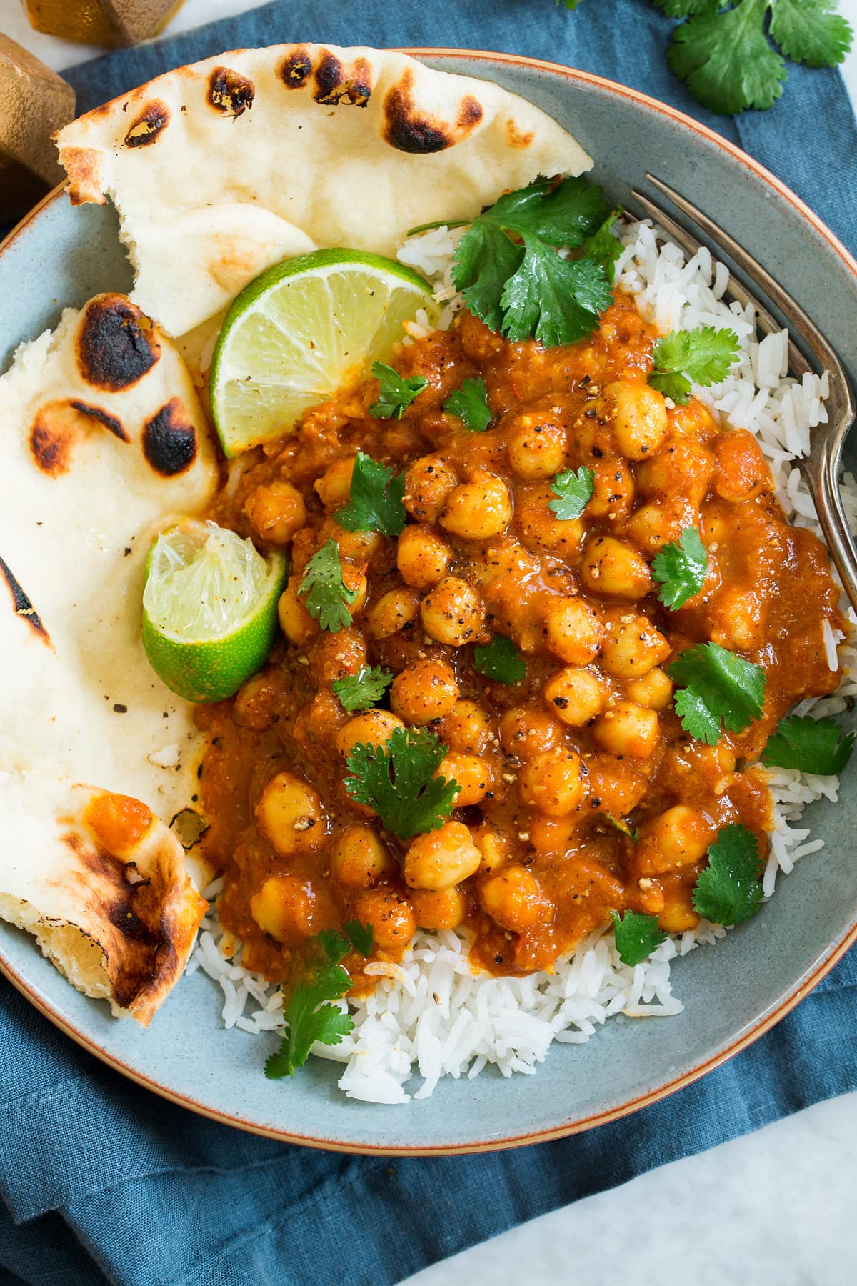 Overhead photo of single serving of chickpea curry with rice, naan, cilantro and limes.