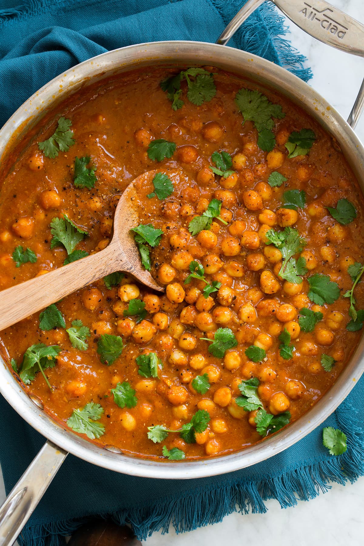 Overhead photo of chickpea curry in a stainless steel pan set over a blue cloth.