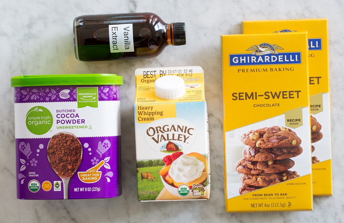 Photo of ingredients used to make homemade chocolate truffles. Includes chocolate bars, heavy cream, vanilla extract, and cocoa powder.