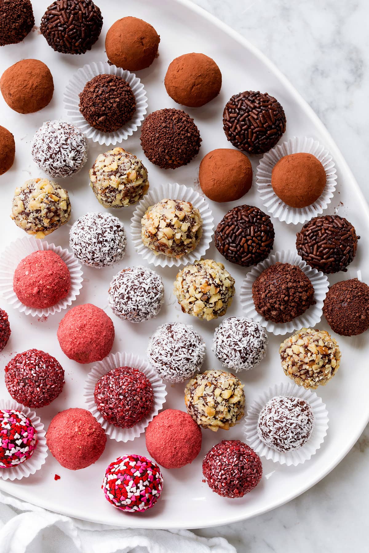 Rows of chocolate truffles coated in different toppings shown on a white oval serving platter.