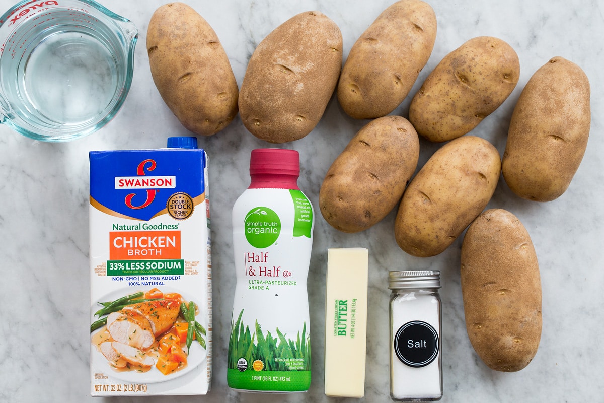 Photo shows ingredients used to make crockpot mashed potatoes. Includes russet potatoes, butter, salt, half and half, chicken broth and water.