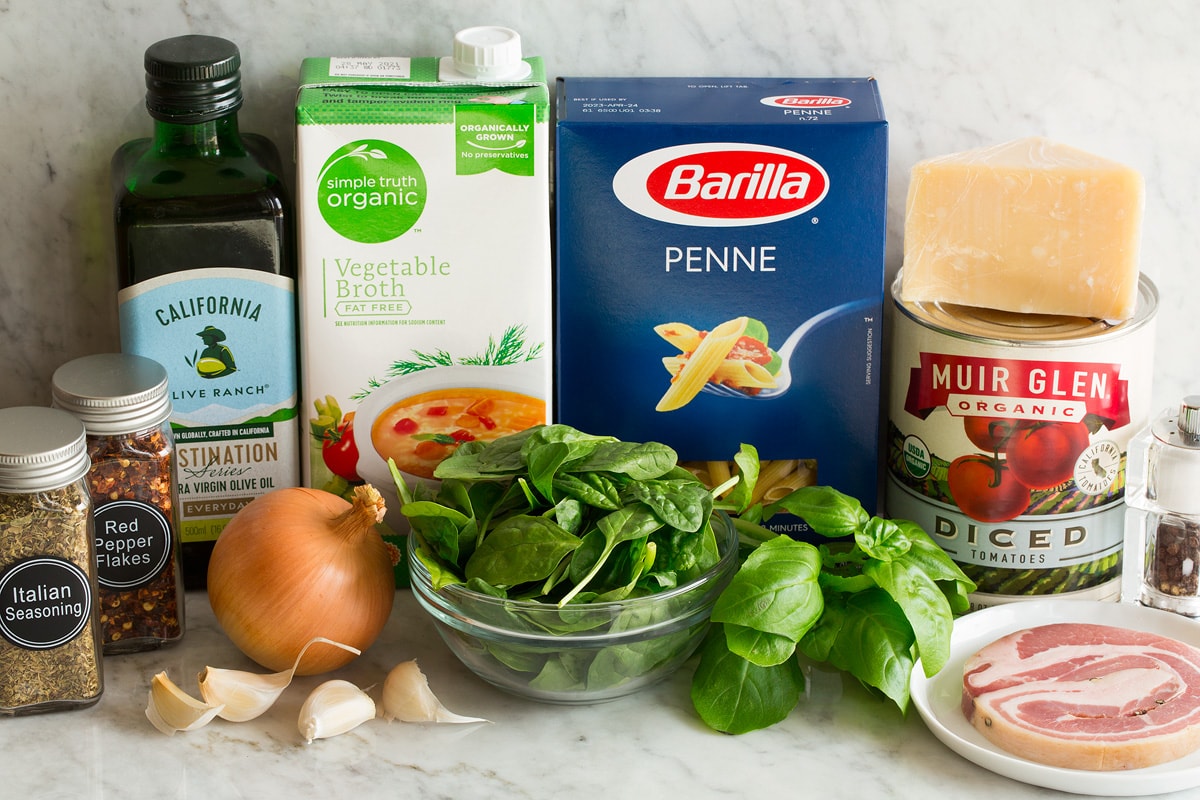 Photo of Ingredients used to make one pot pasta. Includes penne pasta, parmesan, canned tomatoes, spinach, basil, Italian seasoning, pancetta, basil, yellow onion, garlic, red pepper flakes, olive oil and vegetable broth.