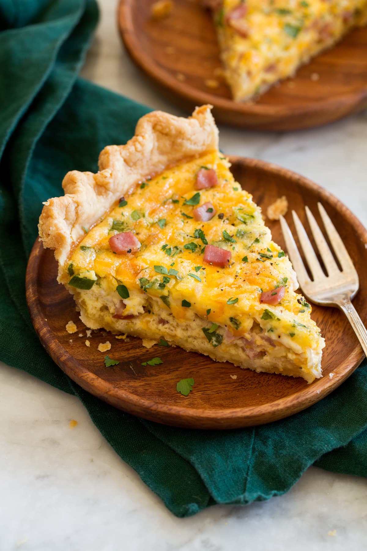 Slice of ham and cheese quiche on a wooden plate set over a green napkin.