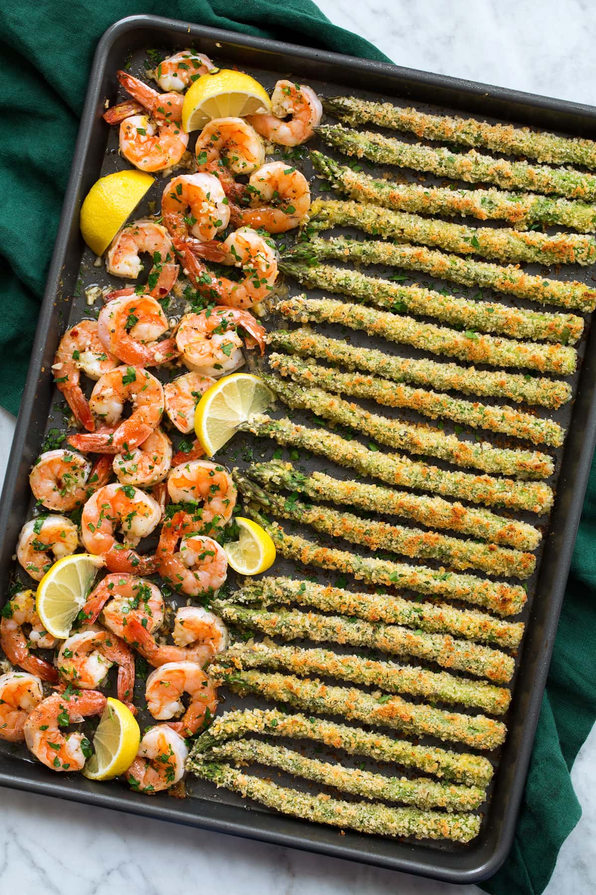 Photo of sheet pan filled with a row of garlic lemon butter shrimp on the left side and panko parmesan crusted asparagus on the ride side. Shown from overhead.