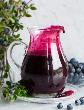 Blueberry syrup in a glass pitcher set over a glass plate.