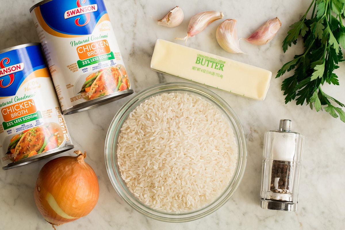 Photo of ingredients needed to make garlic butter rice. Includes white rice, chicken broth, onion, butter, garlic, parsley, salt and pepper.