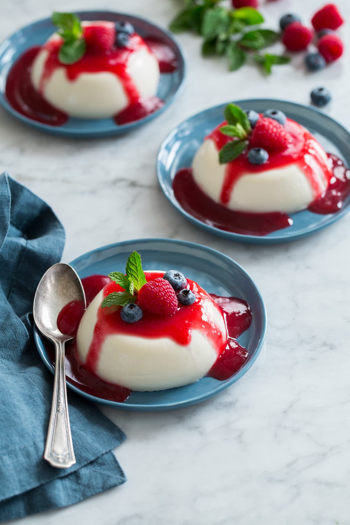 Photo: Three servings of homemade panna cotta shown on dessert plates on a white marble surface.