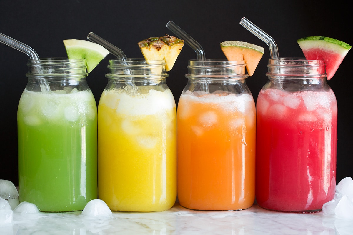 Photo: Four kinds of fruit aqua fresca shown in glass jars with glass straws and fruit wedge garnish.