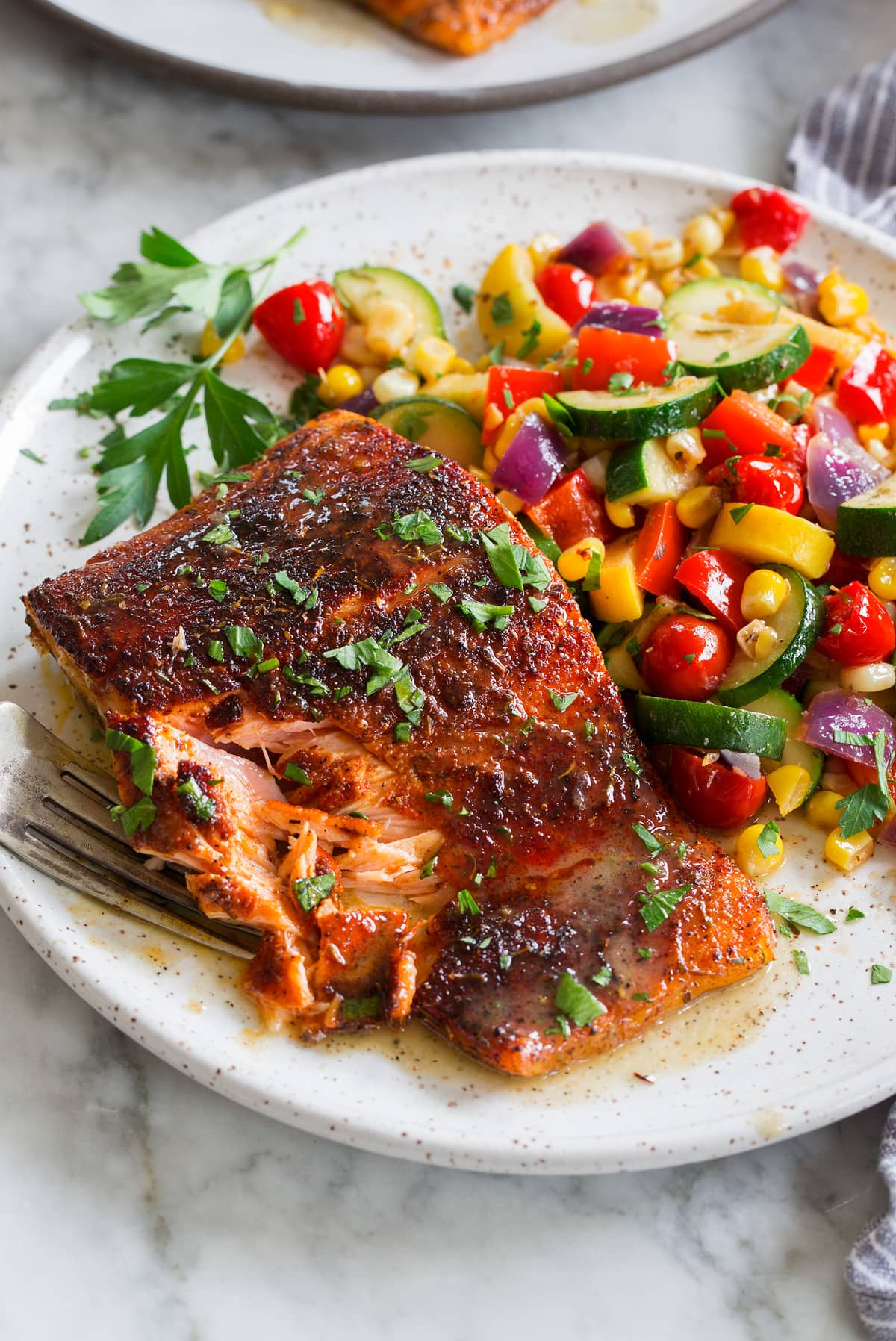 Close up photo of blackened salmon with buttery honey lime sauce. Sautéed vegetables are shown to the side as a serving suggestion.