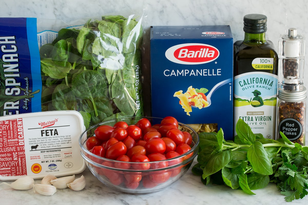 Photo: Ingredients shown that are needed for baked feta pasta. Includes pasta, feta, spinach, basil, parsley, tomatoes, garlic, olive oil, crushed red pepper flakes, salt and pepper.