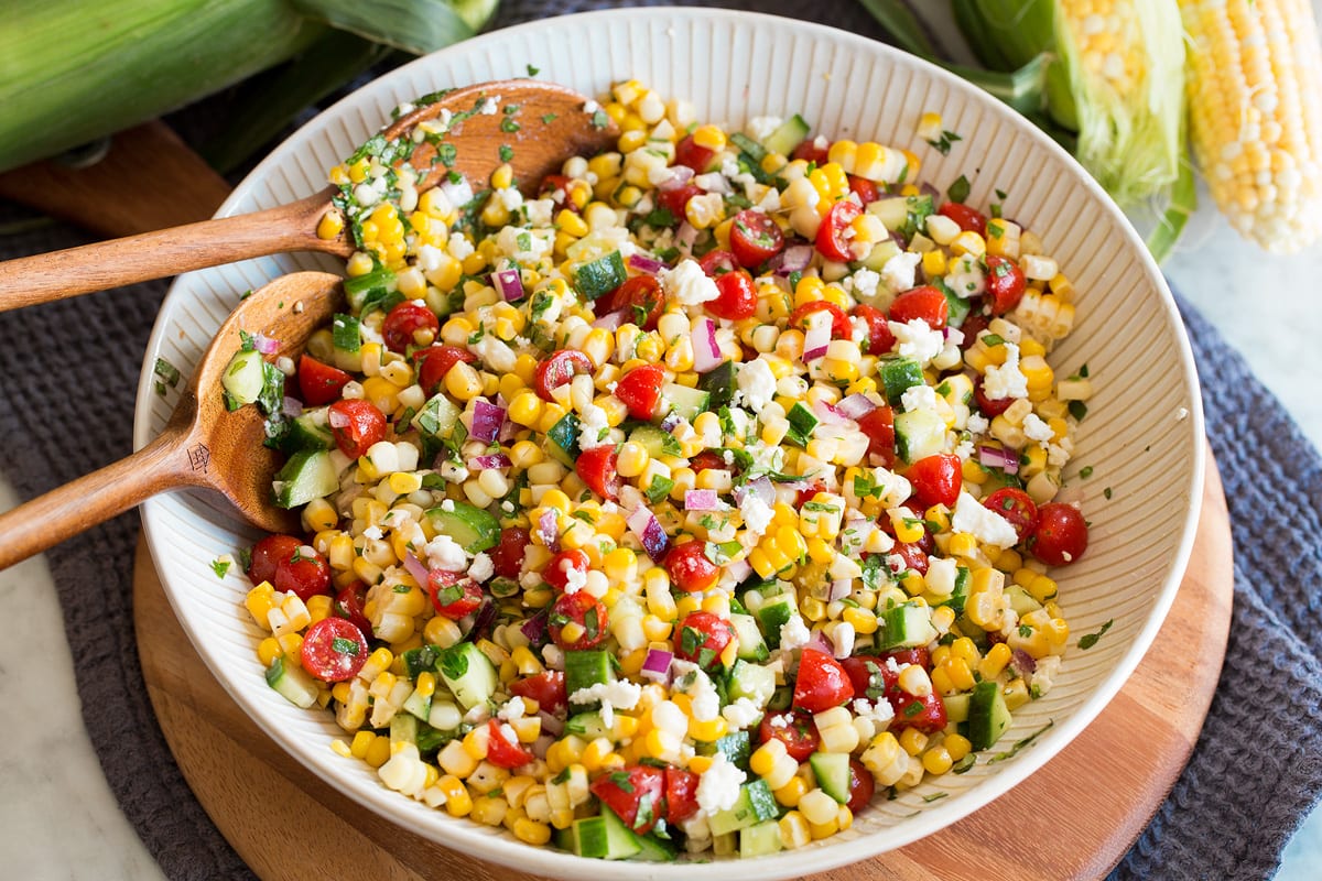 Photo: Completed corn salad after tossing all ingredients and dressing together shown in a white ribbed bowl over a wooden platter.