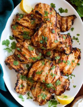 Yogurt Marinated Grilled Chicken shown from above on a white oval platter on a wooden table with a turquoise cloth to the side.