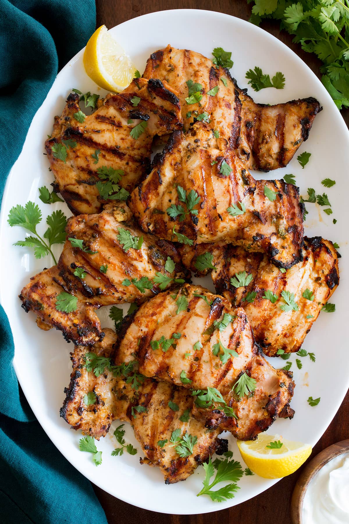 Yogurt Marinated Grilled Chicken shown from above on a white oval platter on a wooden table with a turquoise cloth to the side.