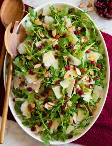 Arugula salad on a white oval platter over a red cloth.