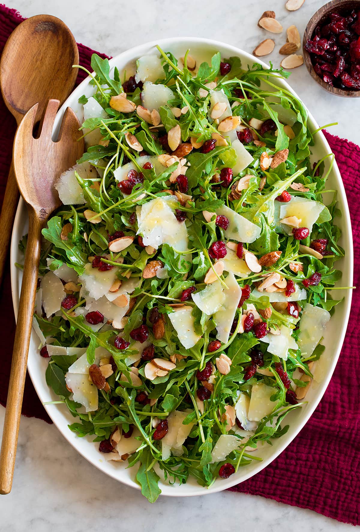 Arugula salad on a white oval platter over a red cloth.