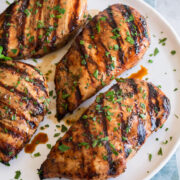 Balsamic chicken breasts shown on a white plate over a blue cloth on a marble surface.