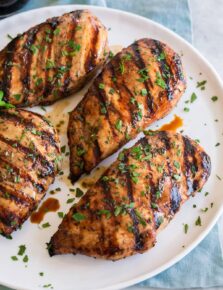 Balsamic chicken breasts shown on a white plate over a blue cloth on a marble surface.