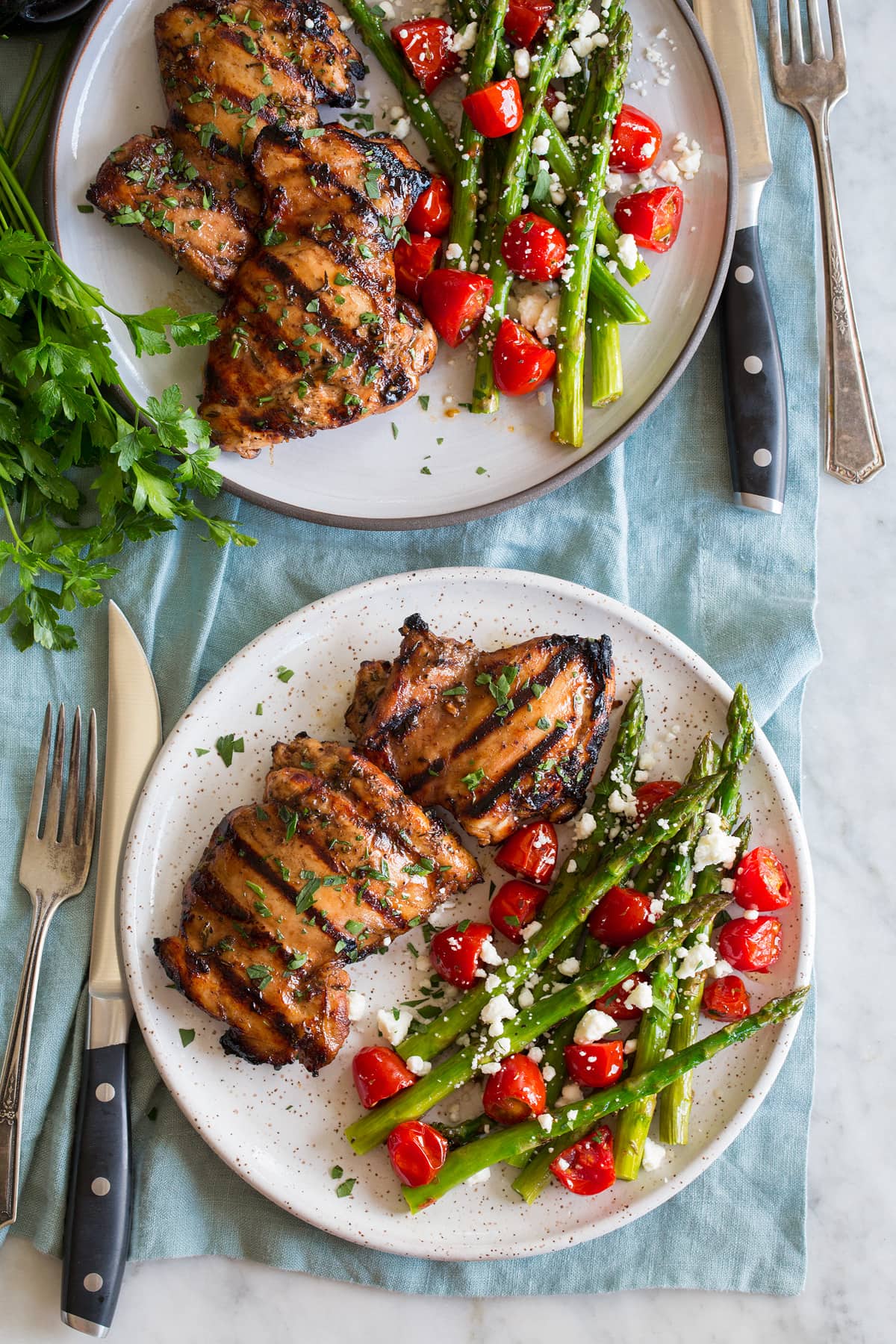 Photo: Two servings of balsamic chicken shown on serving plates with a serving suggestion of roasted asparagus and tomatoes.