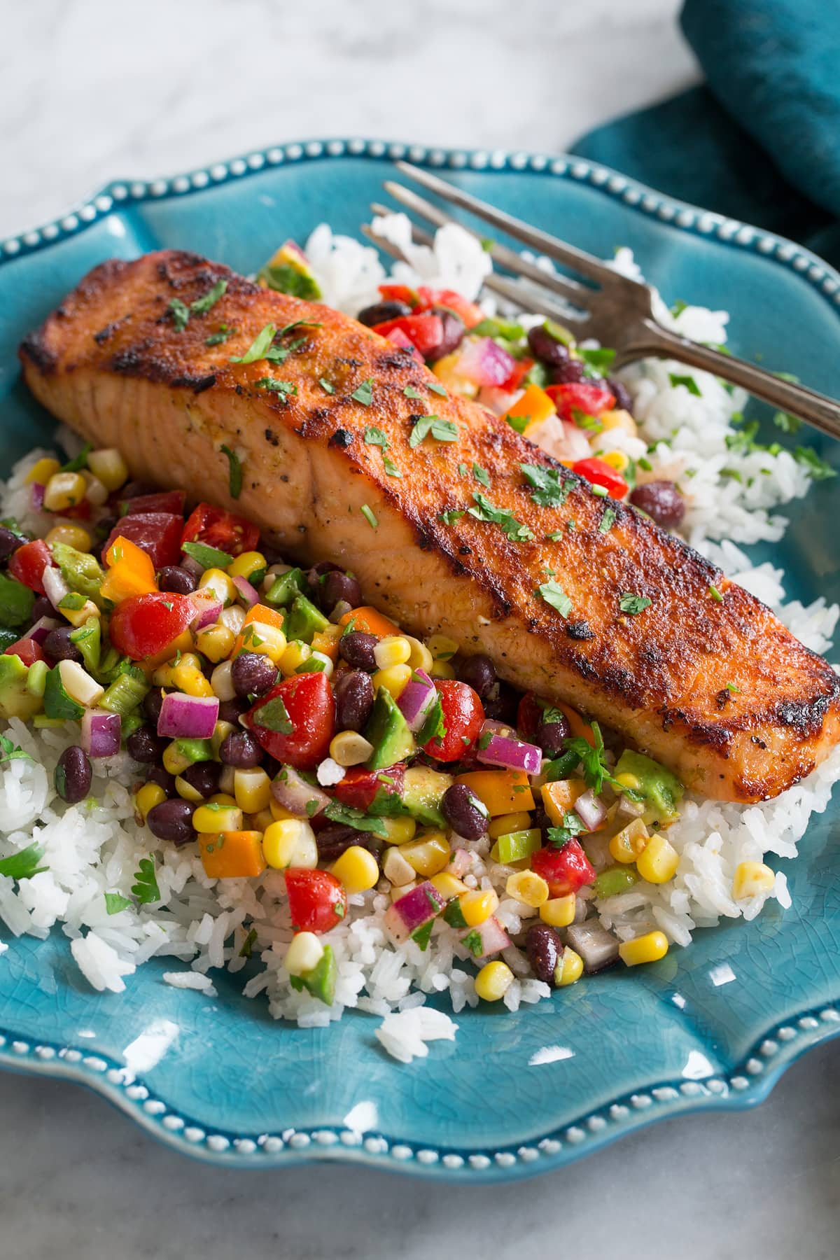 Broiled salmon shown served over a black bean corn salsa and rice on a blue plate.