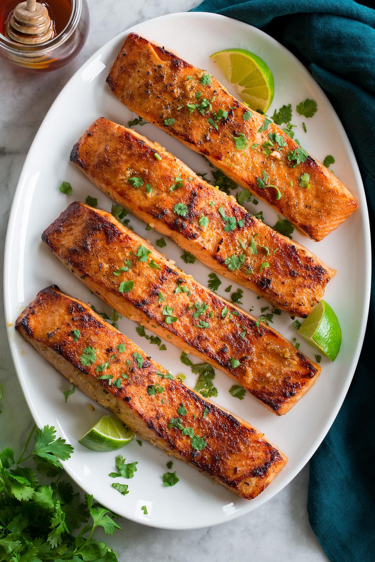 Row of broiled salmon shown from overhead on an a white oval serving platter on a marble surface.