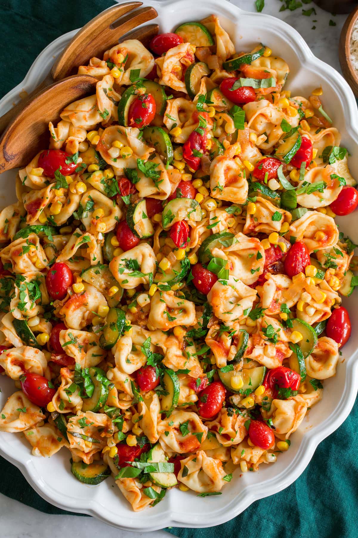 Photo: Overhead image of cheese tortellini and sauteed vegetables shown close up in a white scalloped platter.