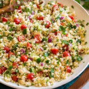 Couscous salad with cucumbers, tomatoes, and herbs shown in a white bowl from the side.