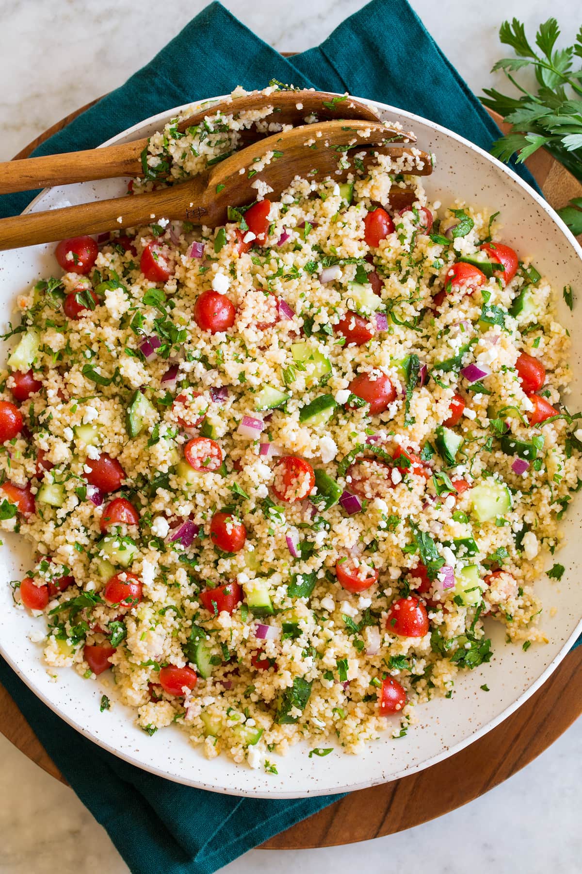 Couscous Salad shown form above in a white ceramic bowl resting on a blue cloth and wooden plate.