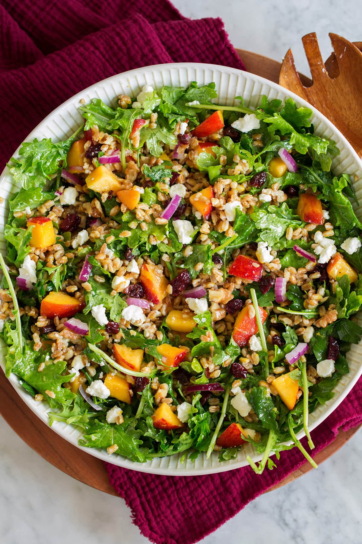 Photo: Farro Salad with peaches, dried cherries, kale, feta and red onion shown in a white serving bowl on a red cloth.