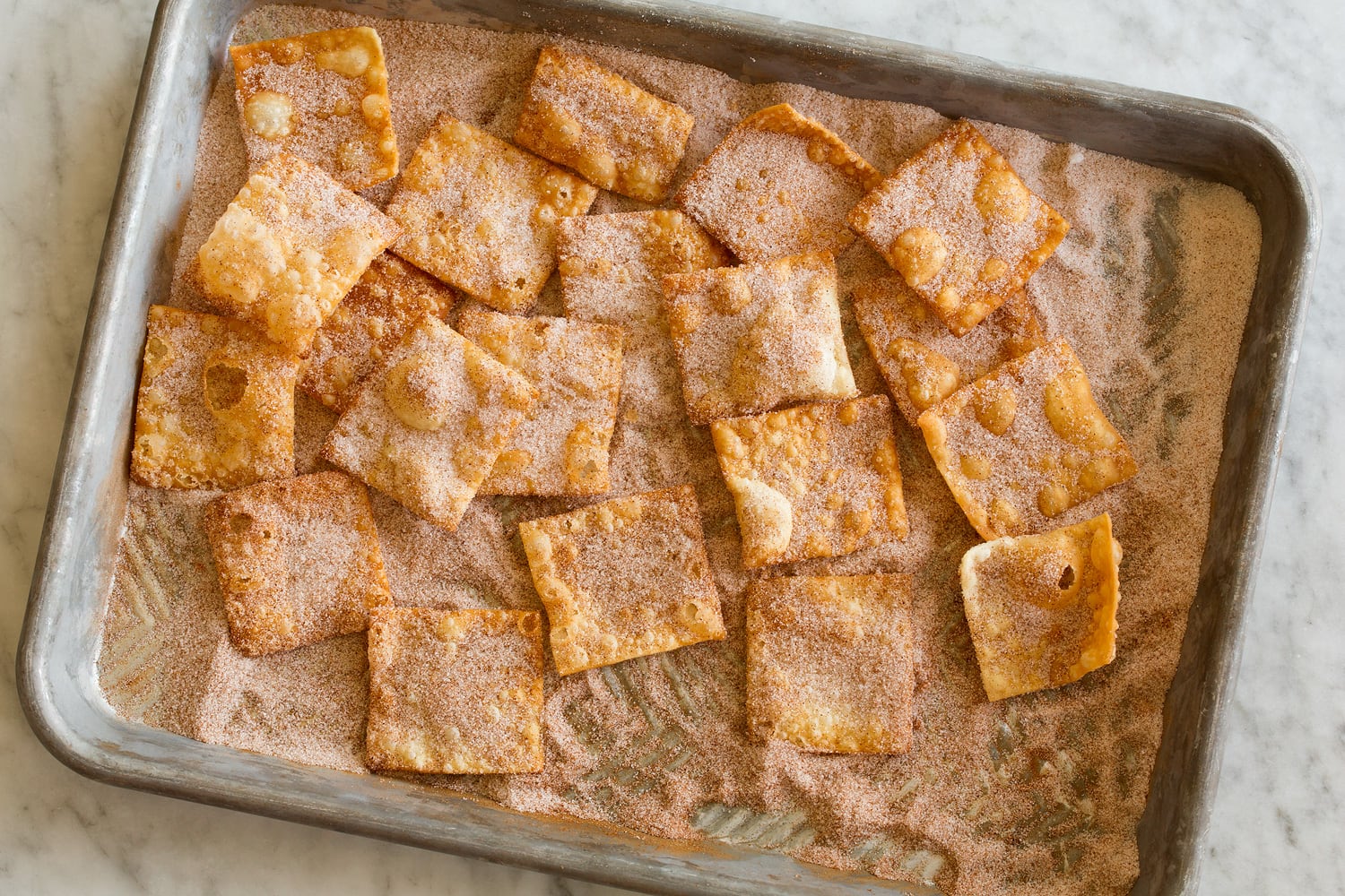 Square wonton chips being tossed with cinnamon sugar.