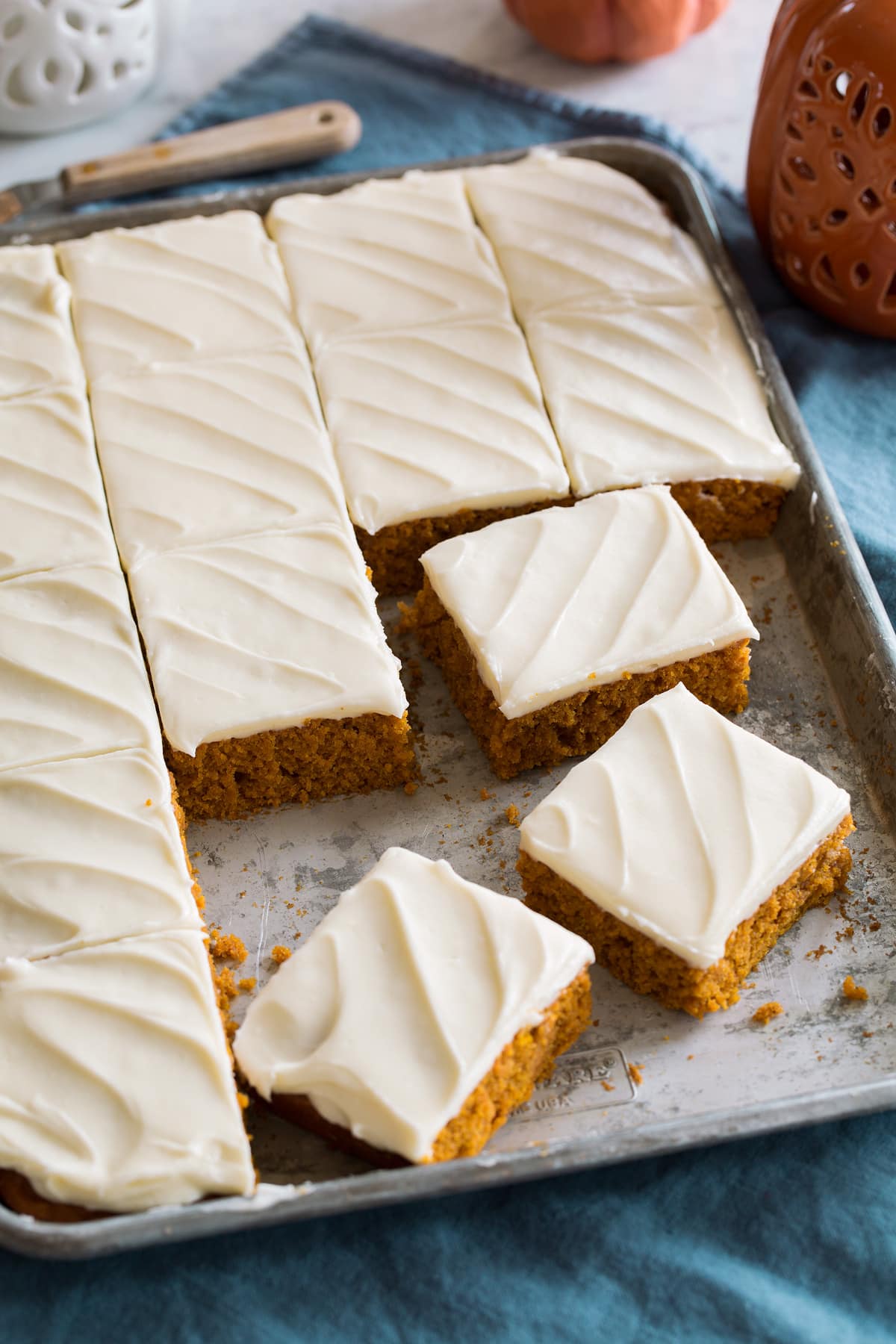 Pumpkin bars with cream cheese frosting cut into squares and shown on a metal sheet pan.