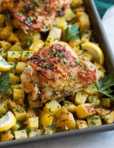 Close up photo of lemon chicken thighs and potatoes on a baking sheet.