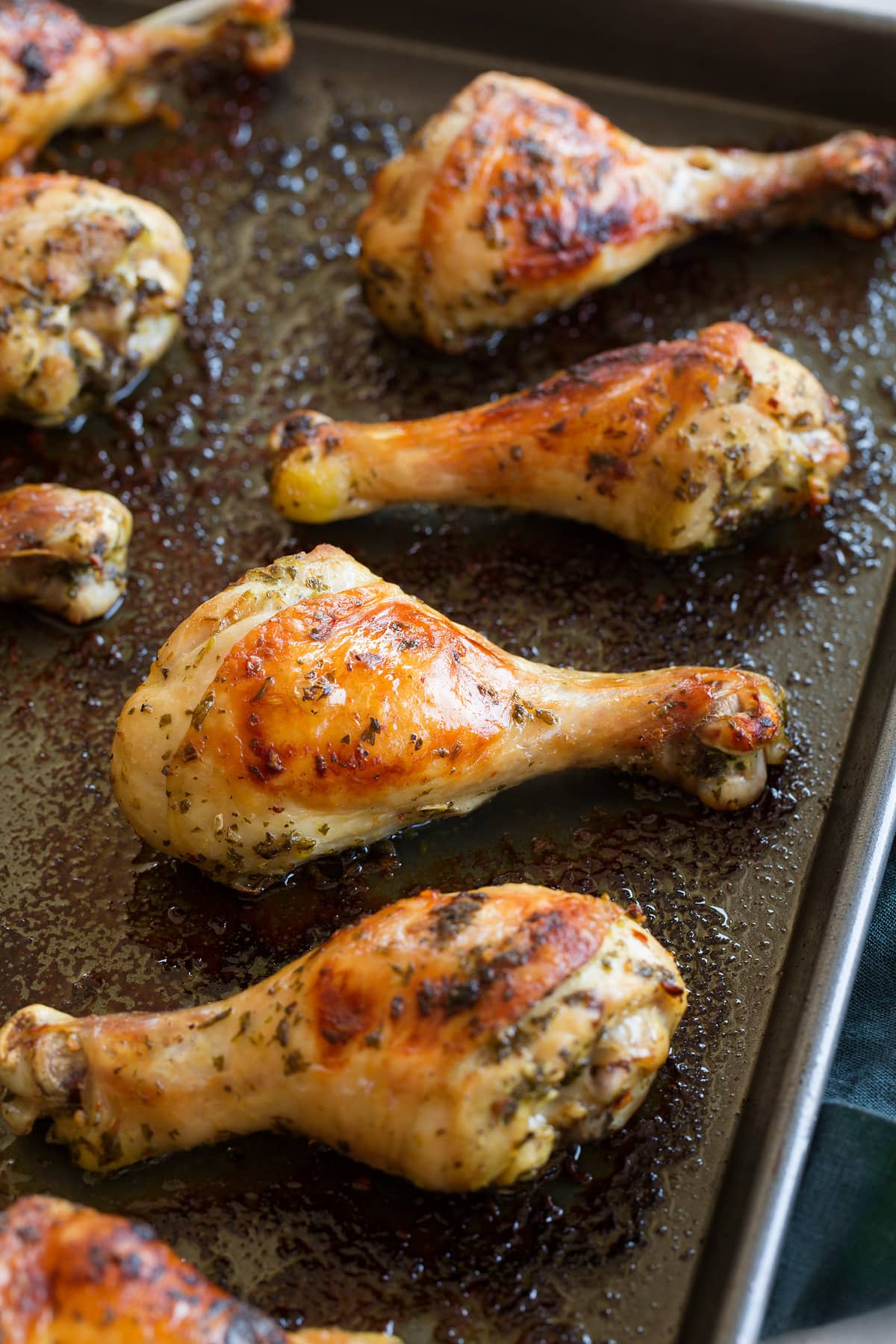 Close up photo of chicken drumsticks on a dark baking sheet.