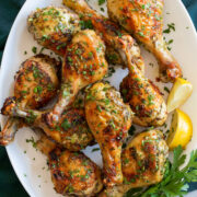 Baked chicken legs on a white oval platter with parsley and lemon wedges to the side.