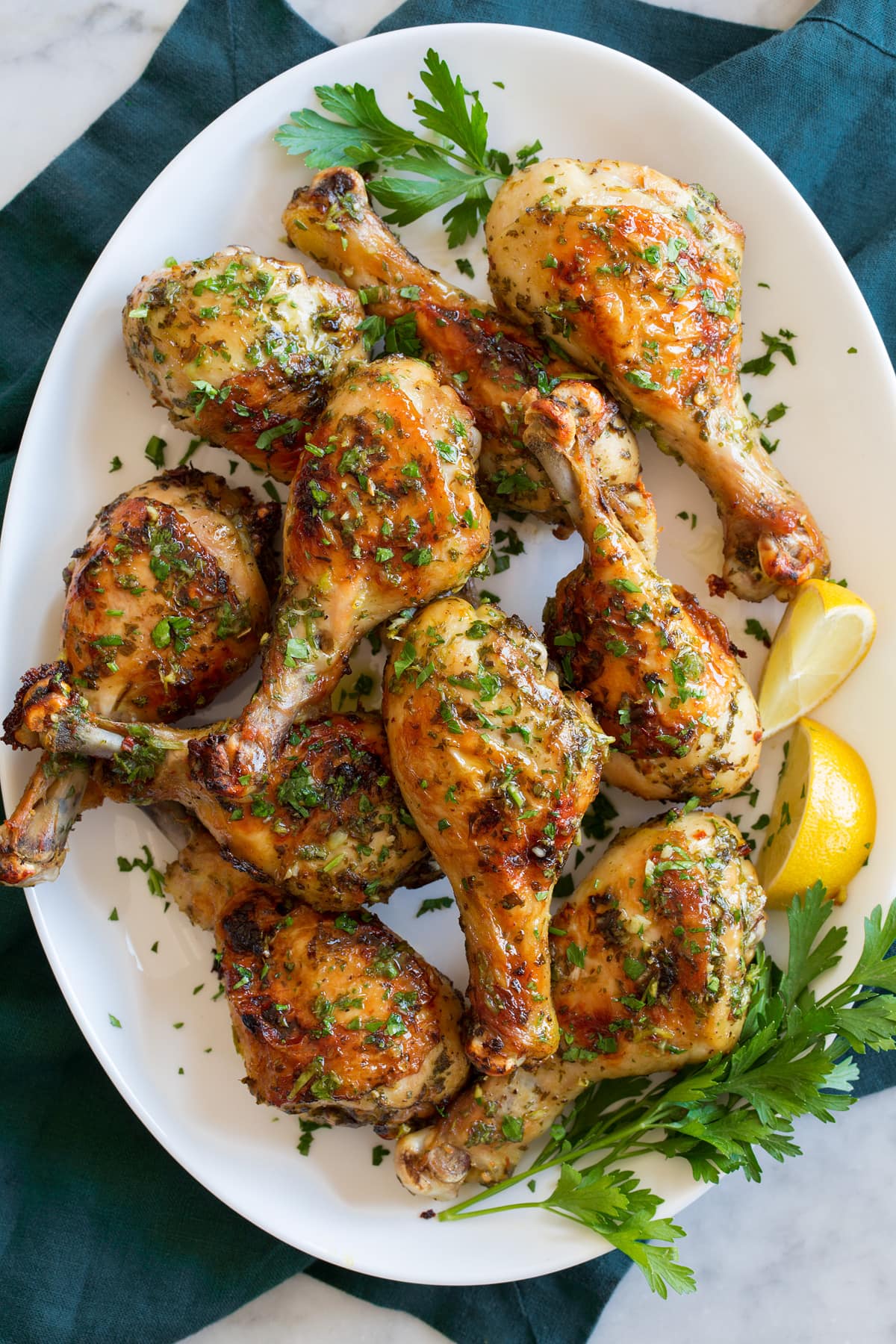 Baked chicken legs on a white oval platter with parsley and lemon wedges to the side.