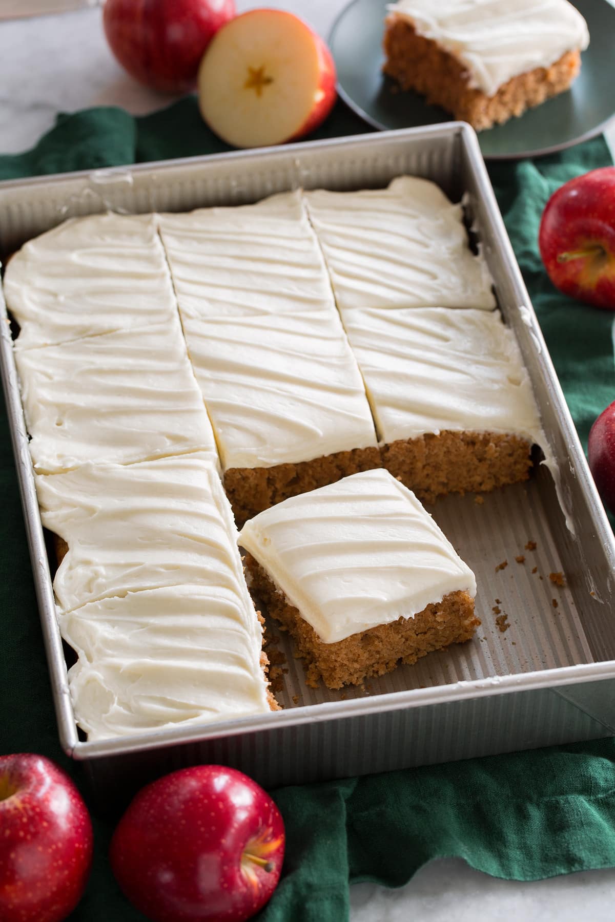 Applesauce cake topped with cream cheese frosting shown in a metal baking sheet over a green cloth.