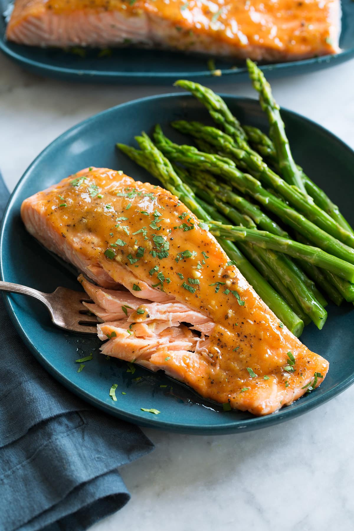 Photo of brown sugar salmon with serving suggestion of steamed asparagus. Served on a blue plate with a blue cloth to the side.