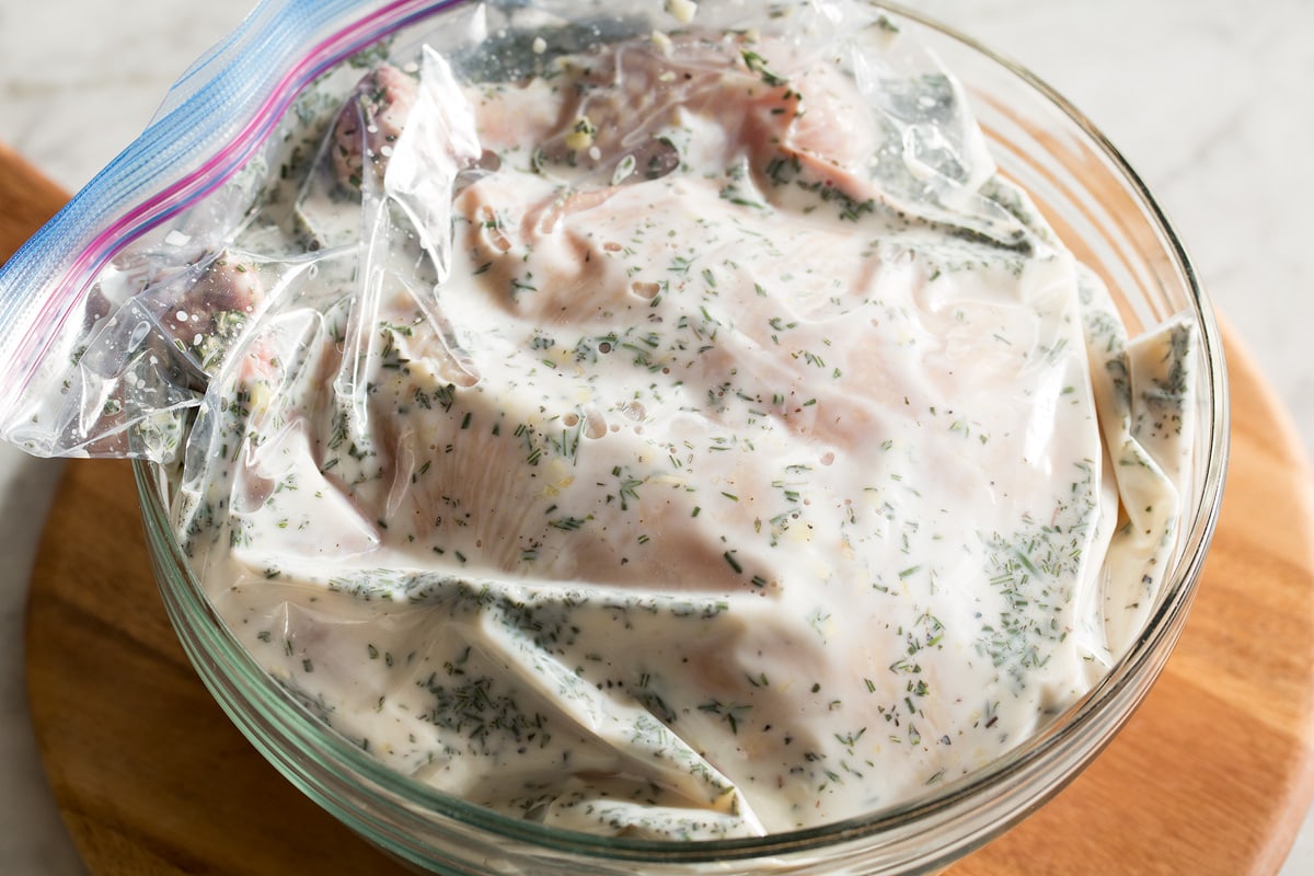 Whole chicken shown in brine in a large bag in a bowl.