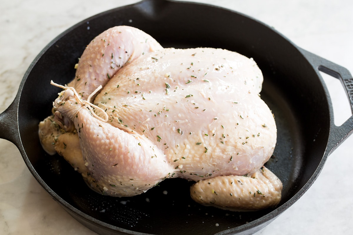 Raw chicken that's legs are trussed in a cast iron skillet before roasting.