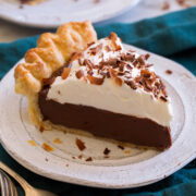 Close up photo of single slice chocolate cream pie that's made with a homemade pie crust, topped with whipped cream and finished with chocolate curls.