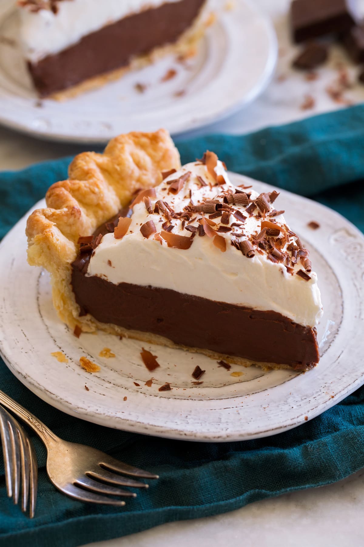 Close up photo of single slice chocolate cream pie that's made with a homemade pie crust, topped with whipped cream and finished with chocolate curls.