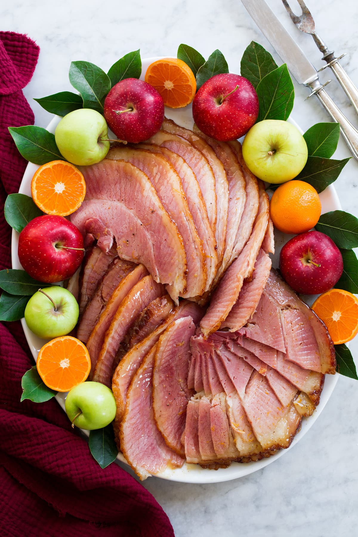 Sliced ham on a platter with fresh fruits and bay leaves.