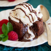 Chocolate lava cake on a serving plate with ice cream on top. Raspberries are shown to the side.