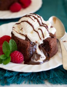 Chocolate lava cake on a serving plate with ice cream on top. Raspberries are shown to the side.