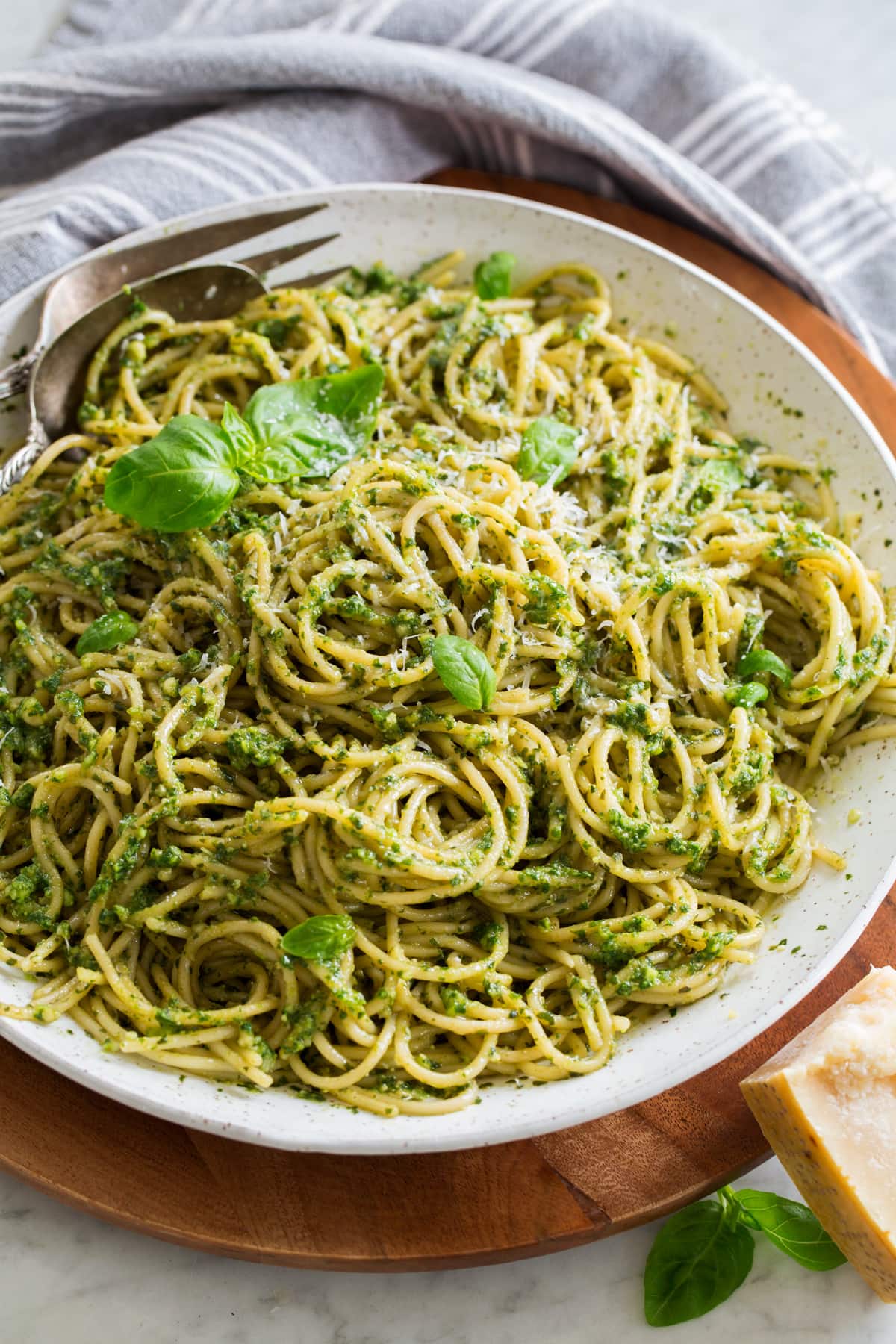 Homemade pesto tossed with spaghetti pasta in a large white serving bowl set over a wooden platter.