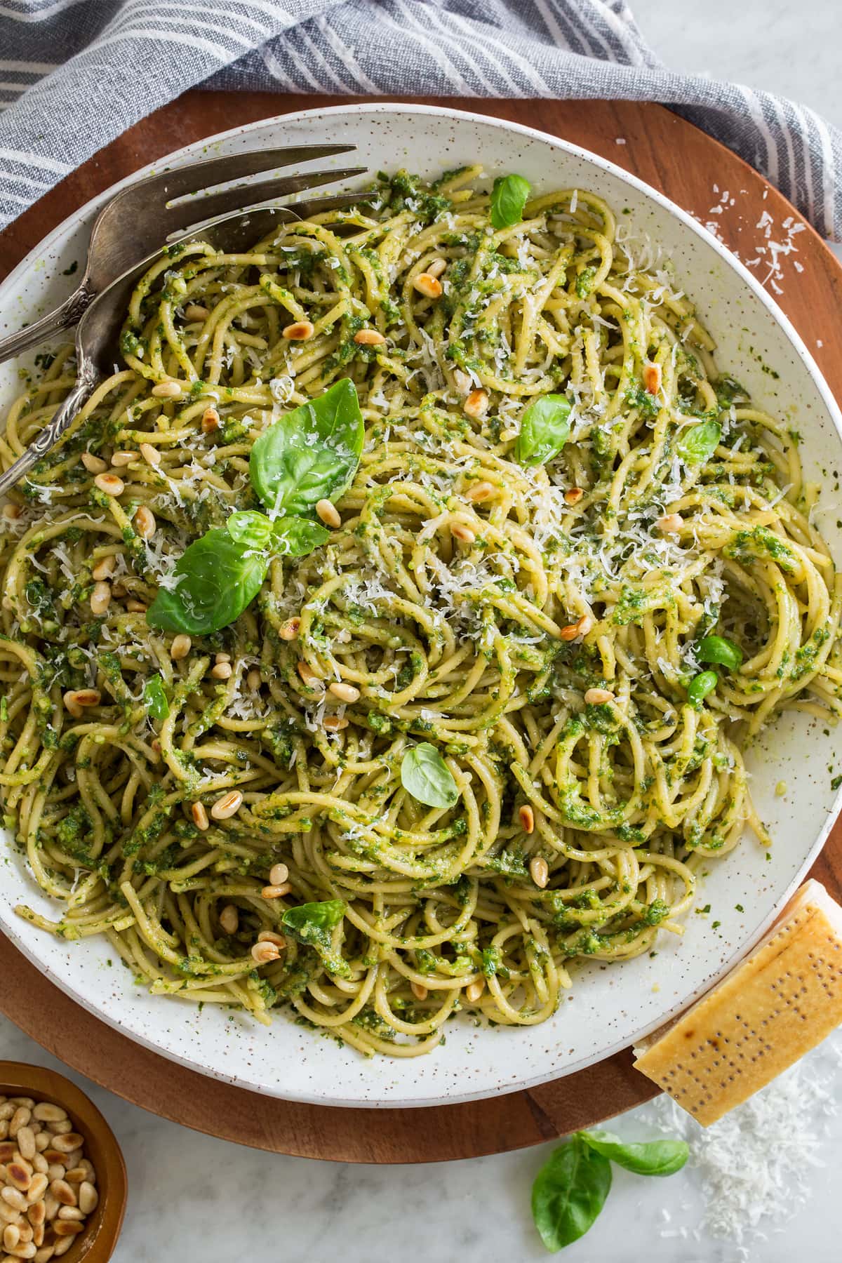 Overhead photo of pesto pasta garnished with basil leaves and toasted pine nuts.