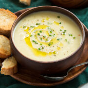 Close up photo of potato leek soup in a wooden bowl garnished with chives and olive oil.