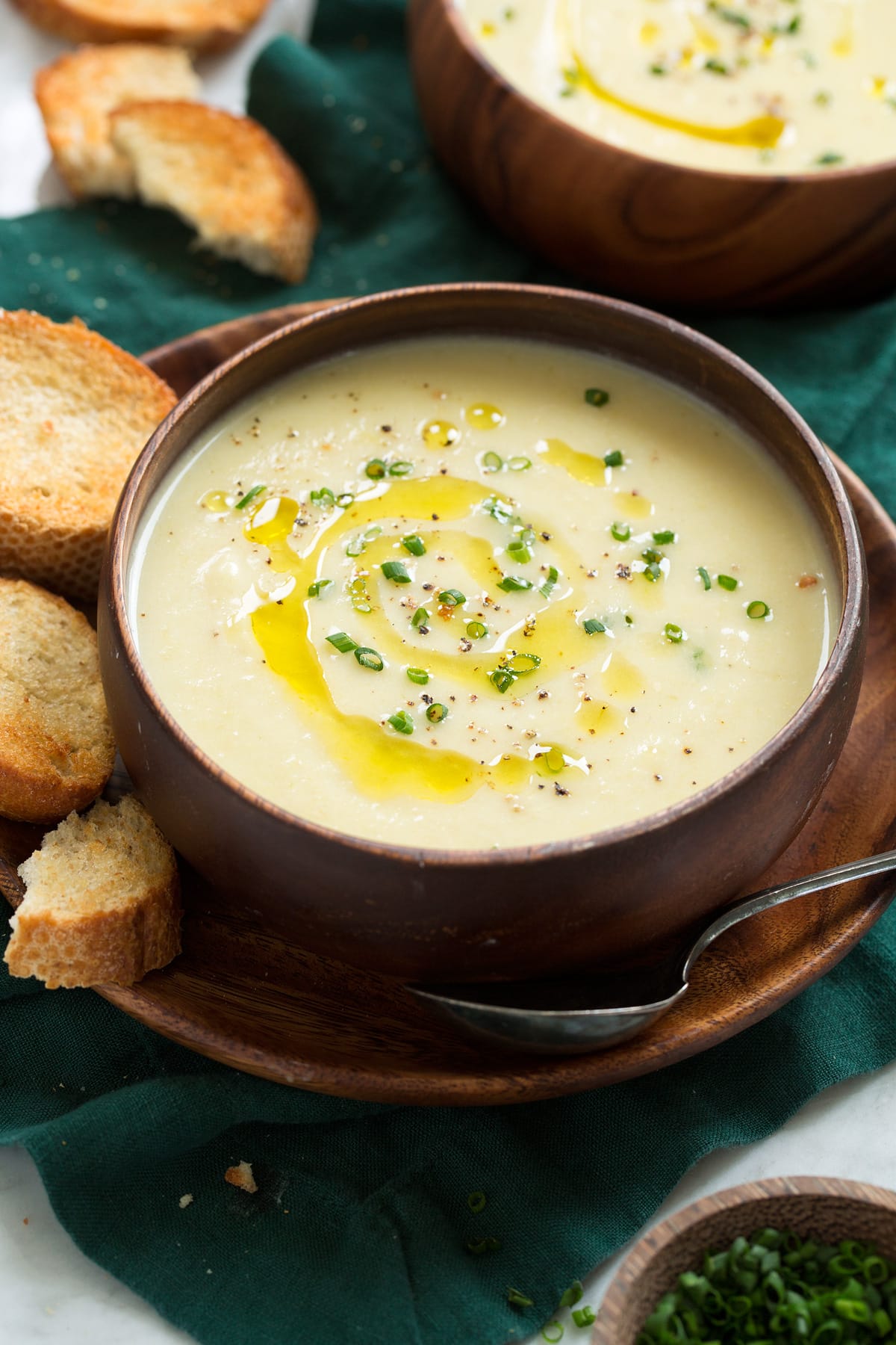 Close up photo of potato leek soup in a wooden bowl garnished with chives and olive oil.