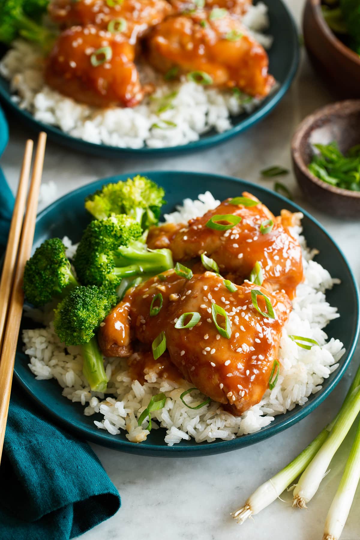 Slow cooker chicken thighs coated in a sauce shown served with white rice and broccoli.