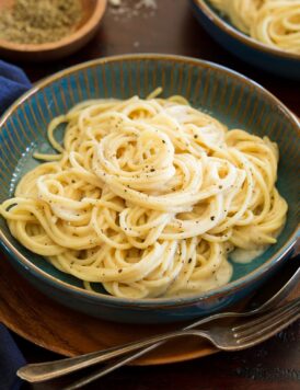 Cacio e pepe in a blue serving bowl over a wooden plate and table.