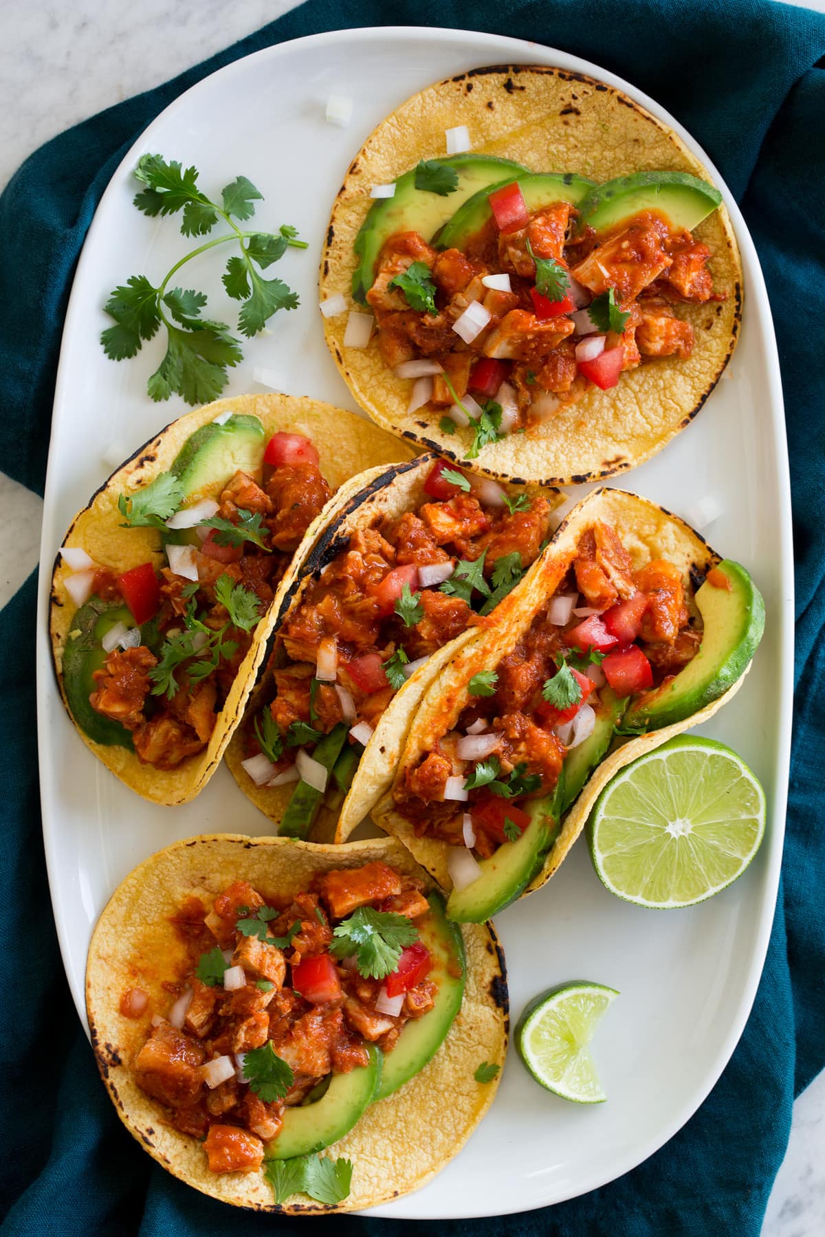 Five chicken tinga tacos on a large white oval platter.